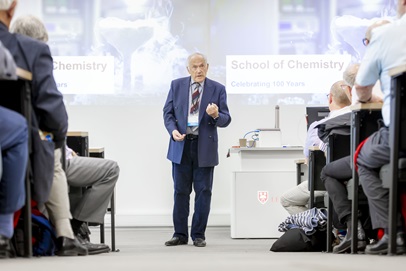Professor Peter Atkins, wearing a blue suit and striped tie. Delivering a lecture highlighting 10 years of Chemistry at Leicester.