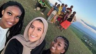 Three midwifery students posing for a photo with patients in the background